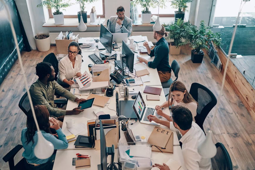 A group of PSS Consulting professionals working together on laptops and documents, demonstrating collaborative teamwork in the office.